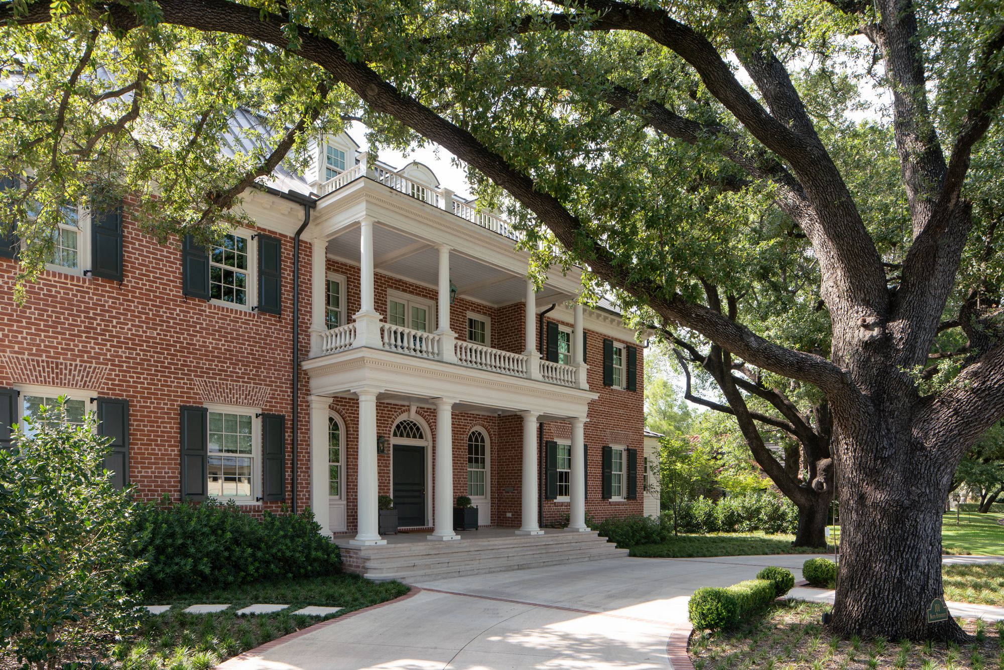 Red brick house with a two-storey porch under a large oak