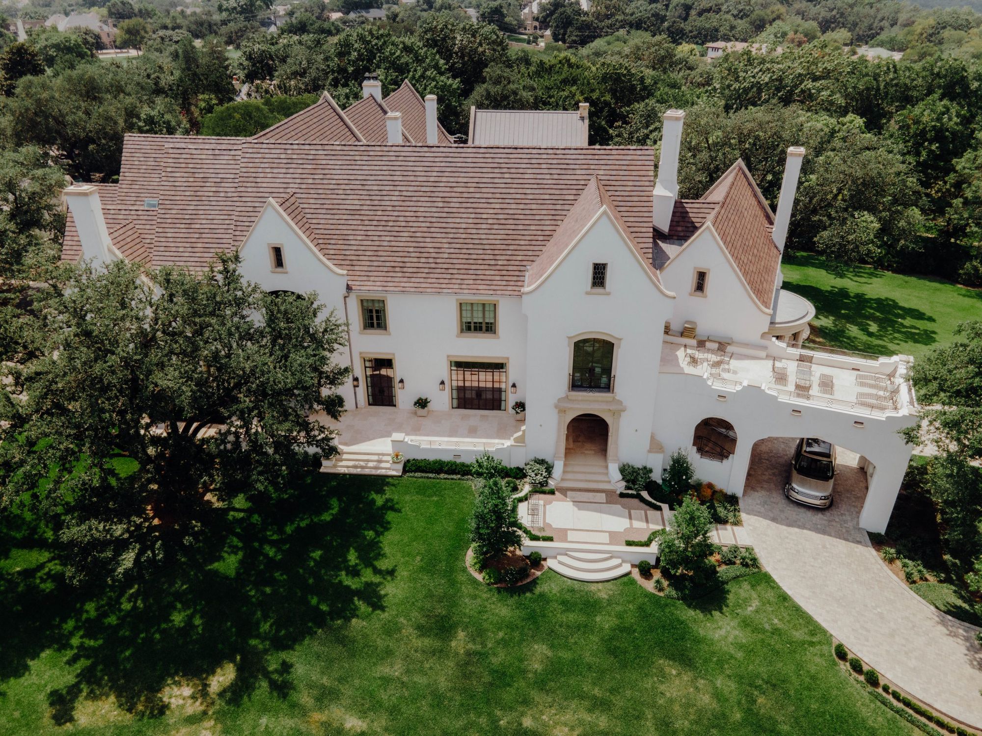 Aerial view of a limewashed house with steep tiled roofs among mature oaks